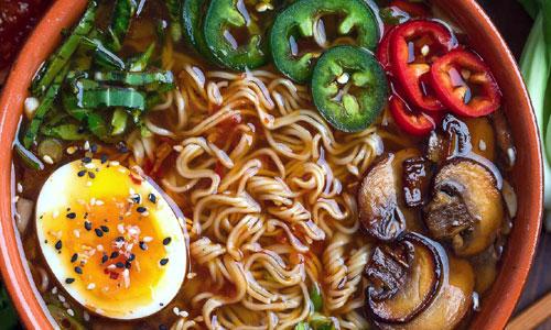 Deep bowl of hot vegetable broth served with wheat noodles and corn